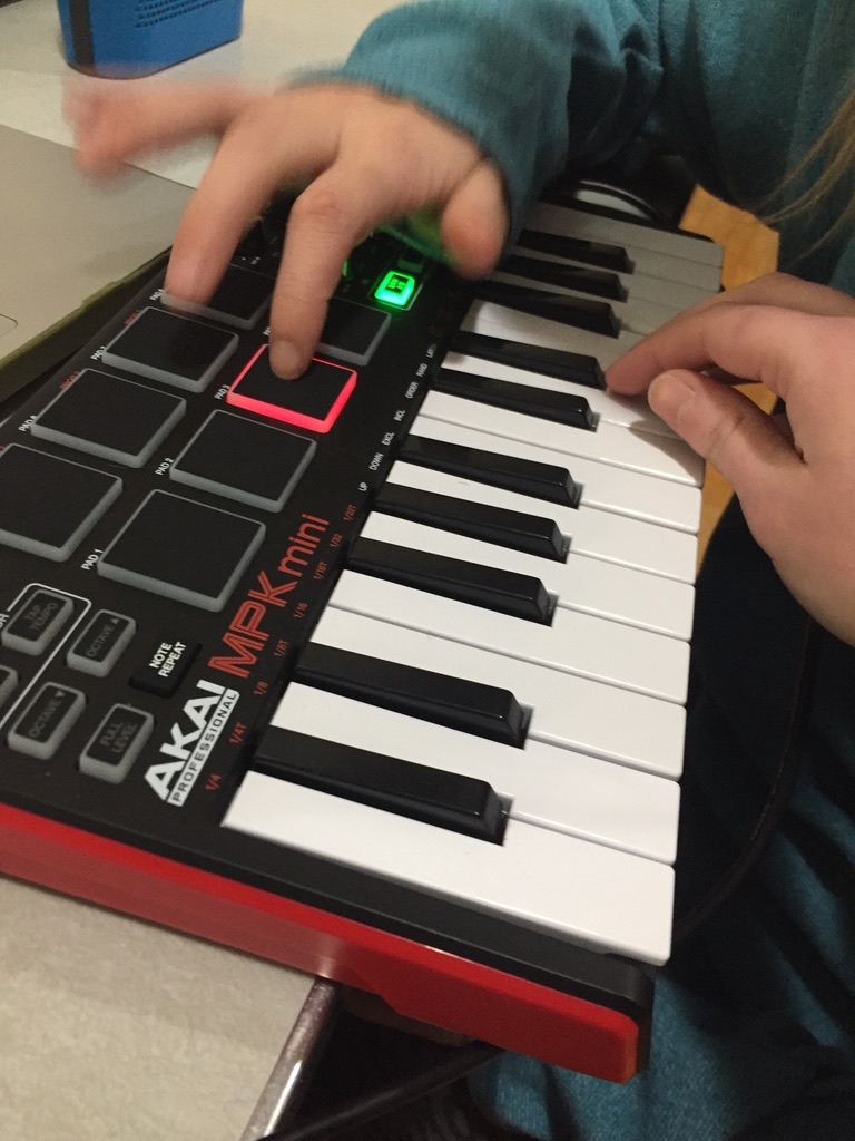 Two hands play a MIDI Keyboard Controller. The child's hand plays the percussive beats and the adult, therapist's hand plays the keyboard.